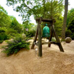 Green bell hanging from wooden garden frame