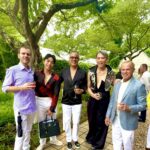 Five well-dressed people outdoors holding drinks