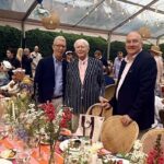 Three men posing by decorated outdoor banquet table
